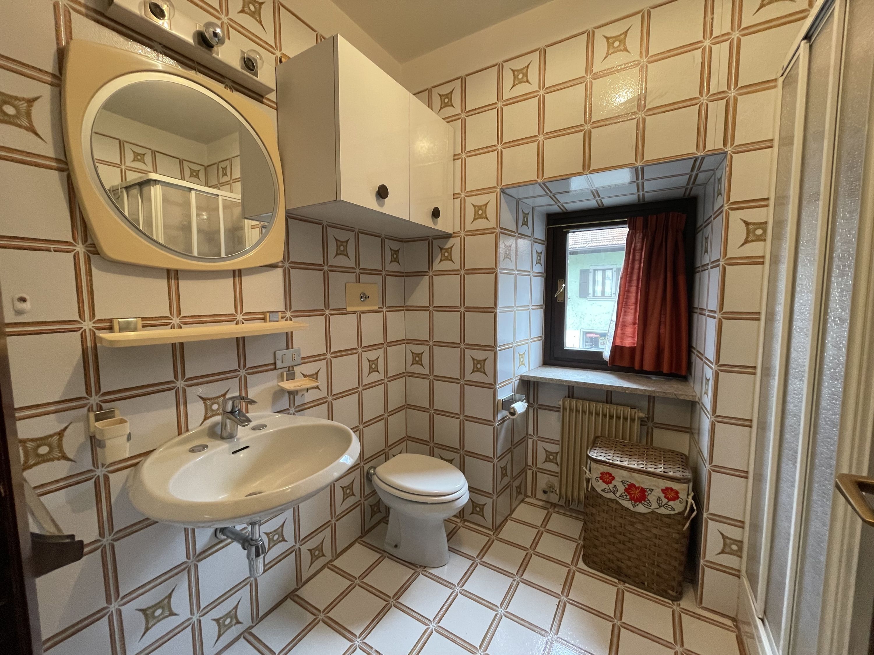 A bathroom with a white sink, a toilet, a mirror, and a window with a red curtain.