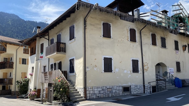 A multi-story building with balconies, a stone staircase, and a sign indicating a public area. - 020 Trilocale Pinzolo (Pinzolo)