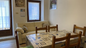 A dining area with a table set for four, a wooden chair, a sofa, and a window with curtains. - 020 Trilocale Pinzolo (Pinzolo)