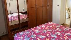 A bedroom with a wooden wardrobe, a bed with a floral bedspread, and a mirror cabinet. - 020 Trilocale Pinzolo (Pinzolo)