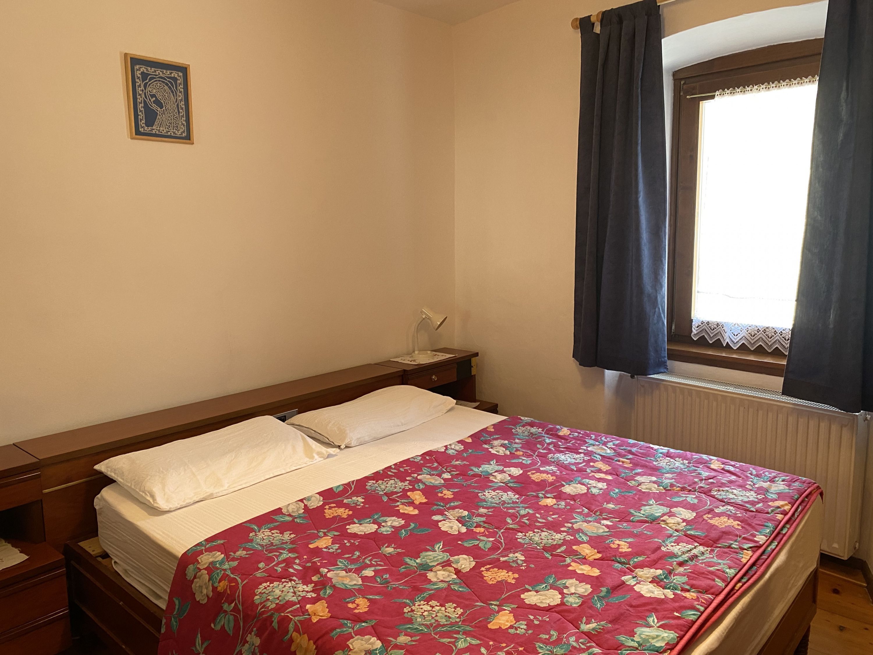 A bedroom with a bed, a nightstand, a window with curtains, and a wall-mounted picture.