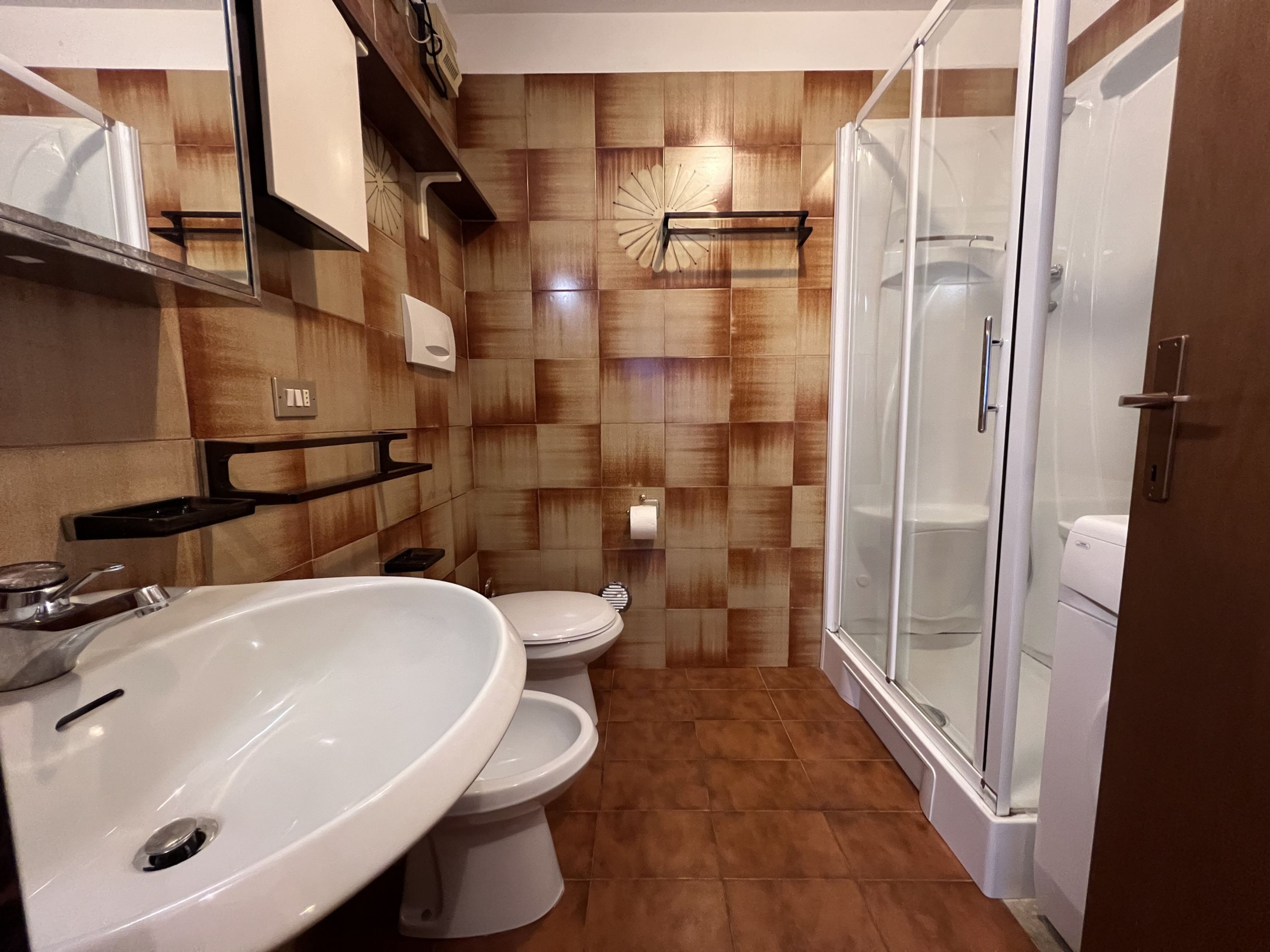 A modern bathroom with a large white sink, two toilets, and a glass-enclosed shower.