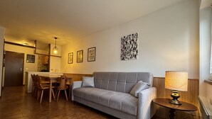 Ein Wohnzimmer mit grauem Sofa, einem Holztisch und einem Essbereich mit Tisch und Stühlen.