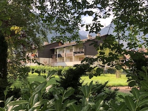 Ein zweistöckiges Gebäude mit Balkon, umgeben von viel Grün und blauem Himmel.