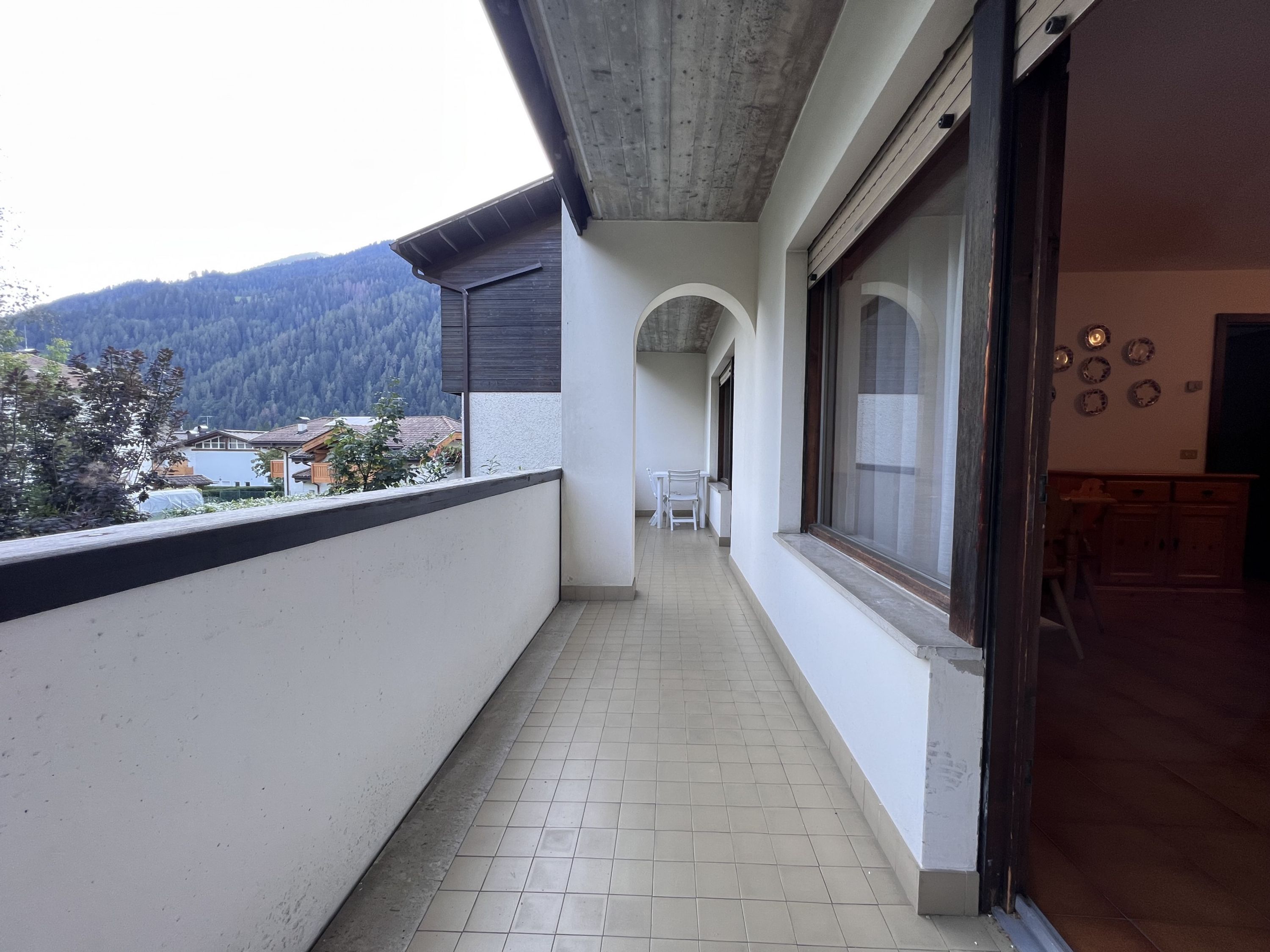 A corridor with tiled flooring, a view of a mountainous landscape, and a dining area with chairs and a table.