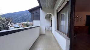 A corridor with tiled flooring, a view of a mountainous landscape, and a dining area with chairs and a table. - 040 Bilocale Pinzolo (Pinzolo)