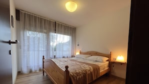 A bedroom with a wooden bed, white curtains, a bedside lamp, and a ceiling light. - 040 Bilocale Pinzolo (Pinzolo)