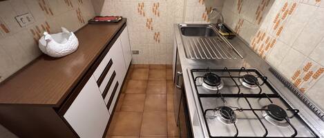 A compact kitchen with a gas stove, a sink, and a decorative white bird on the counter.