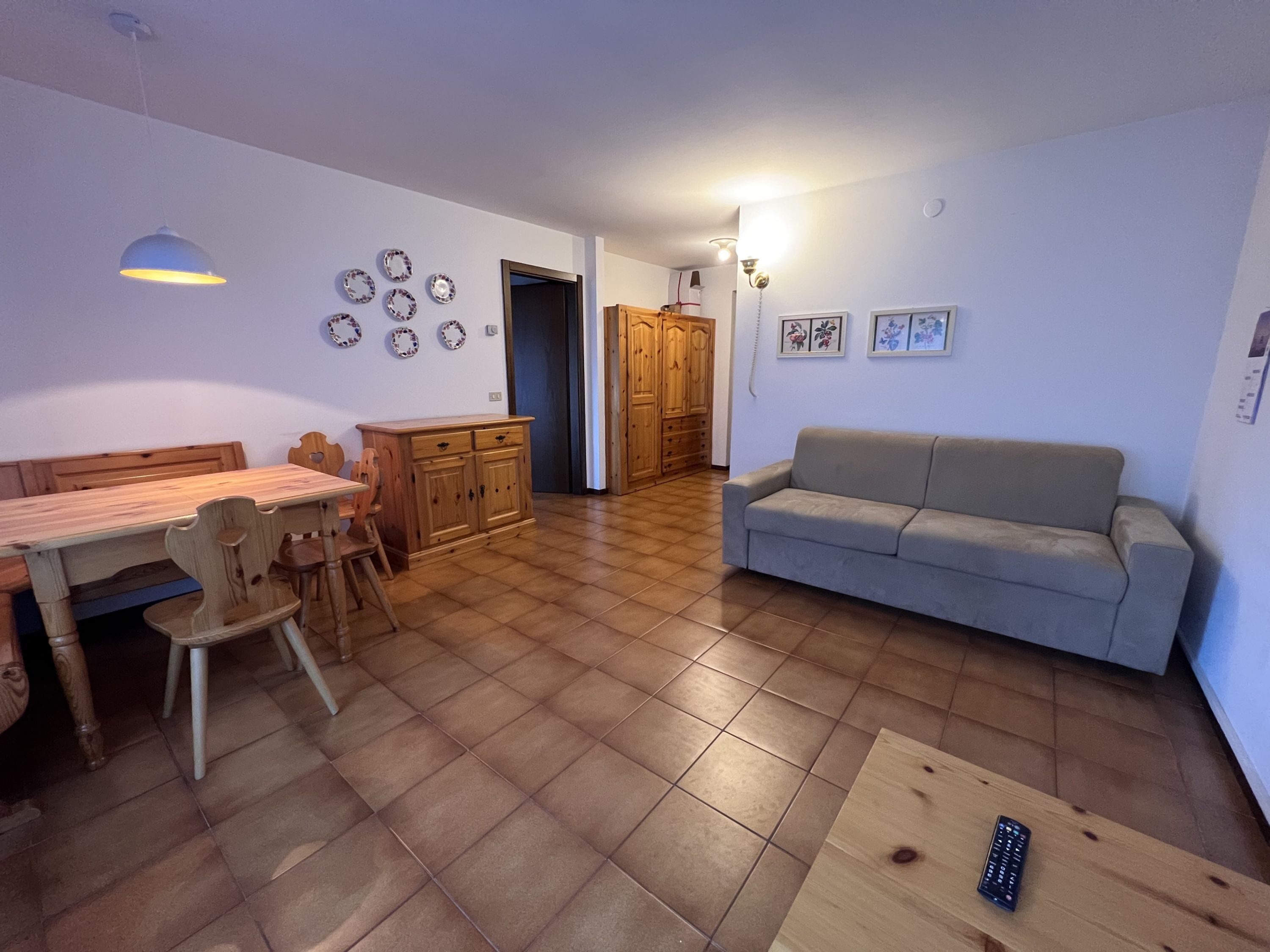 Un amplio salón con una mesa de comedor de madera, sillas, un sofá gris y un mueble de madera.