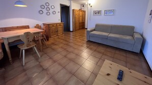 A spacious living area with a wooden dining table, chairs, a grey sofa, and a wooden cabinet. - 040 Bilocale Pinzolo (Pinzolo)
