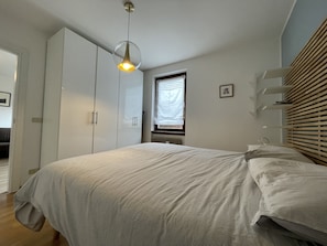 A bedroom with a bed, a wardrobe, a window with blinds, and a hanging light fixture. - 034 Trilocale Pinzolo (Pinzolo)