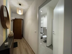 A hallway with a wooden floor, a mirror, a pendant light, and a door leading to a bathroom with a toilet and sink. - 034 Trilocale Pinzolo (Pinzolo)