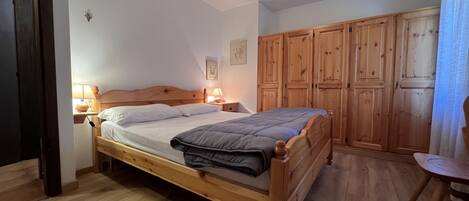 A bedroom with a wooden bed, bedside lamps, a wooden wardrobe, and a small table.