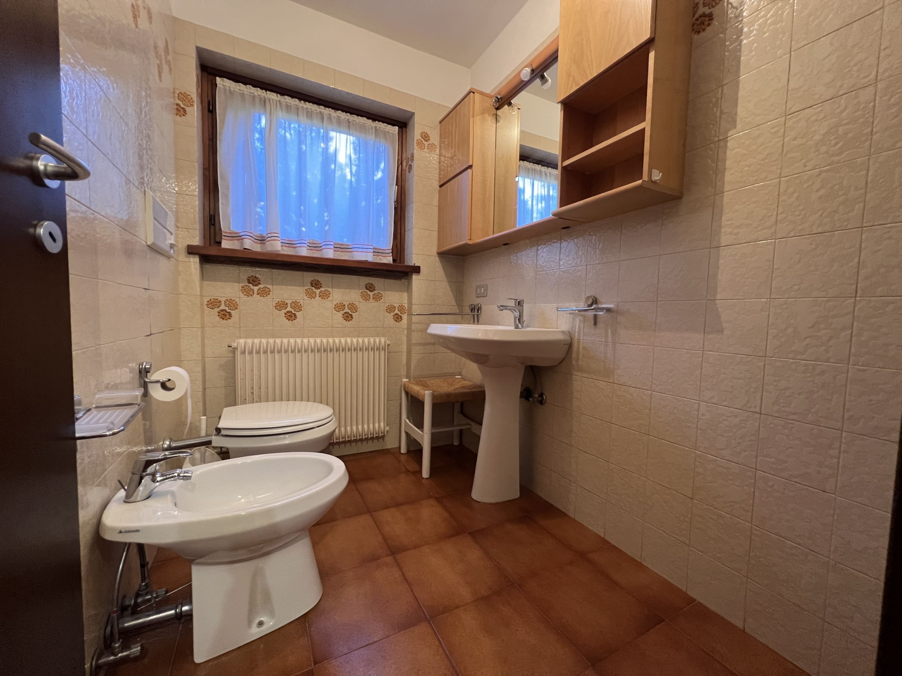 Une salle de bain comprenant des toilettes, un bidet, un lavabo et une fenêtre avec des rideaux.