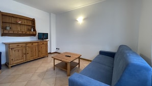 A living room with a blue sofa, wooden cabinet, and a television on a stand. - 090 Cond Gaiolin 22 (Giustino)