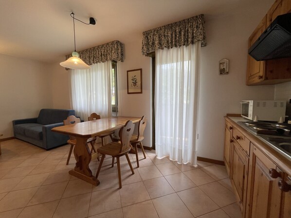 A dining area with a wooden table and chairs, a blue sofa, and a kitchen with a microwave. - 090 Cond Gaiolin 22 (Giustino)