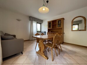 Uma área de refeições com mesa e cadeiras de madeira, um sofá, um armário com portas de vidro e um lustre.