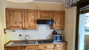 A kitchen with wooden cabinets, a stainless steel sink, a gas stove, and a microwave. - 091 Cond Gaiolin 23 (Giustino)