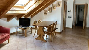 A cozy attic room with a wooden dining table, chairs, a TV, and a red sofa. - 092 Cond Gaiolin 27 (Giustino)