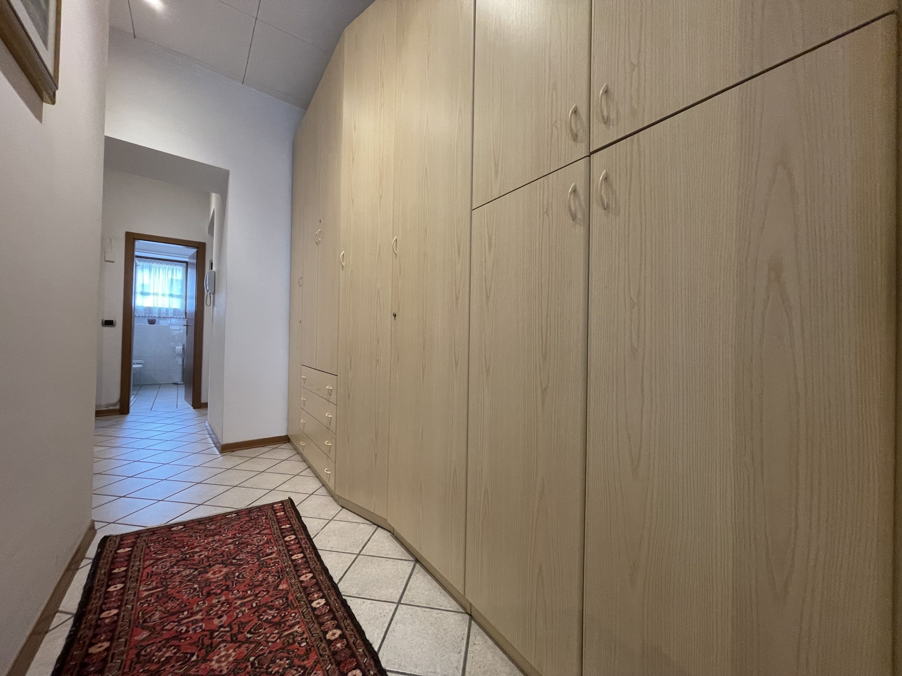 A hallway with a large wardrobe, tiled floor, and a patterned rug.