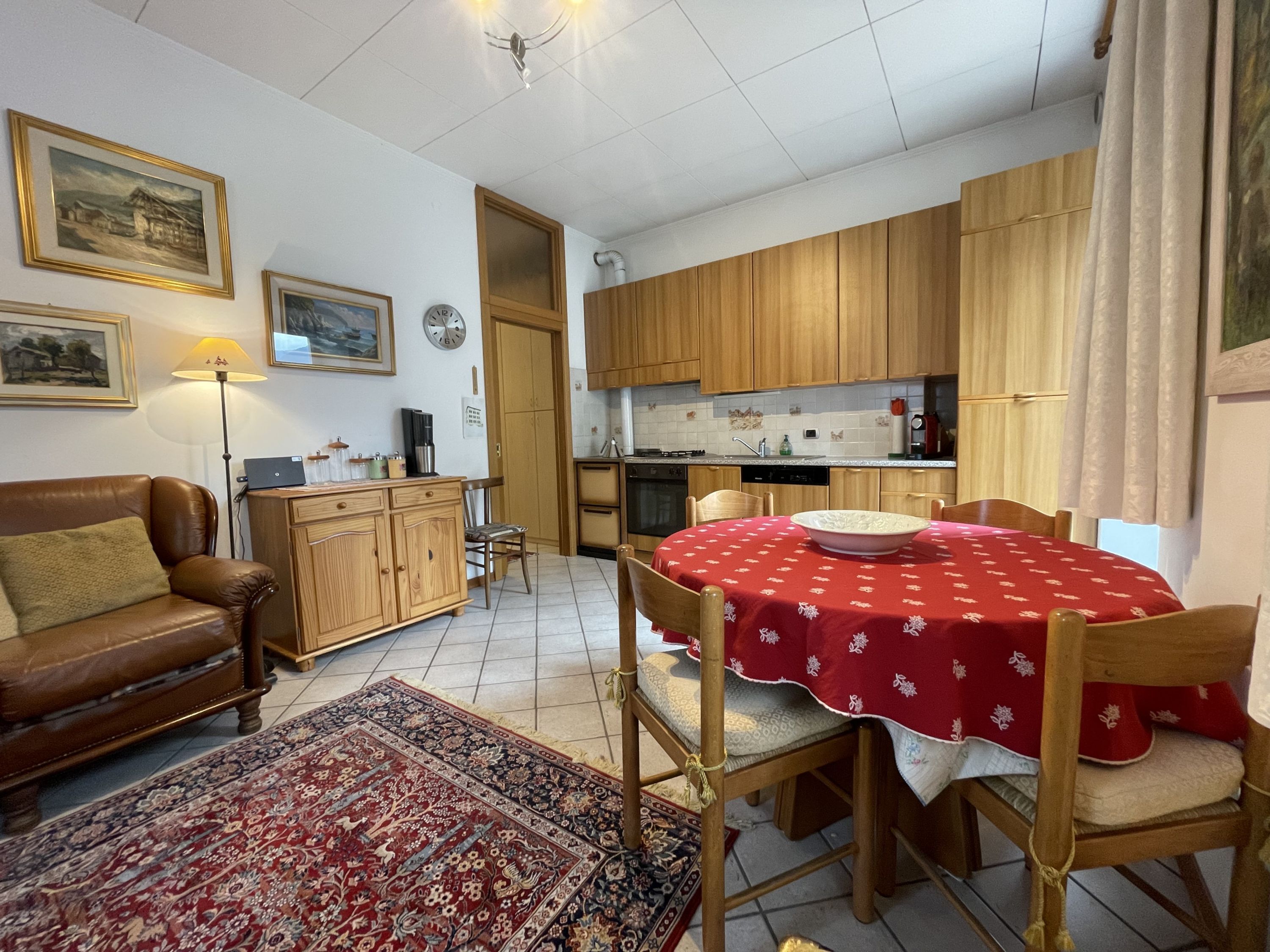 Un salón acogedor con un sofá de cuero marrón, una mesa de comedor con mantel rojo y una cocina con armarios de madera y salpicadero de azulejos.