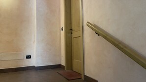 Egy folyosó, amelyen egy fa ajtó, egy korlát és egy fali lámpa található.
