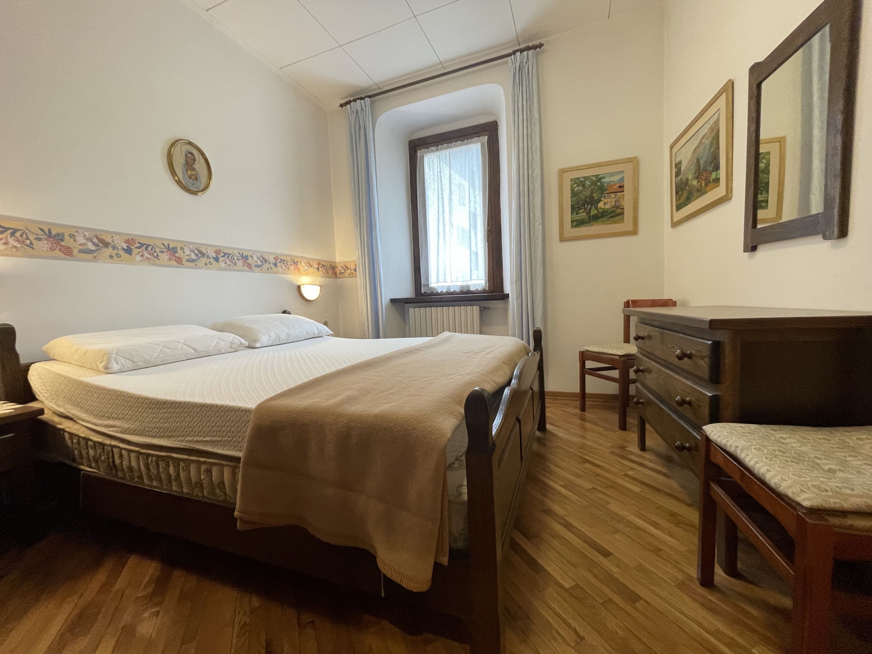 Un dormitorio con cama, cómoda de madera y ventana con cortinas.
