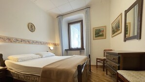 Egy hálószoba, amelyben egy ágy, egy fa komód és egy függönnyel ellátott ablak található.