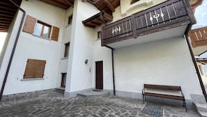 Un edificio con patio empedrado de piedra, balcones de madera y un banco.
