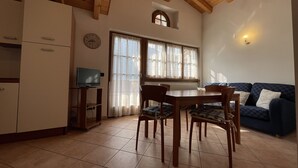 Una sala de estar acogedora con una mesa de comedor y sillas, un sofá, un televisor sobre un mueble bajo y un reloj en la pared.