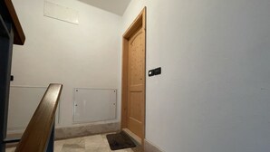 Un pasillo con una puerta de madera, un portero automático negro y un piso de baldosas.