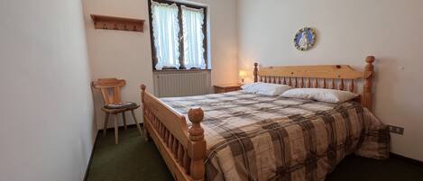 A bedroom with a wooden bed, a chair, a window with curtains, and a wall decoration.