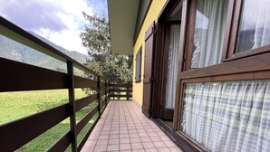 A balcony with a tiled floor, wooden railing, and large windows with curtains. - 071 Bilocale Pinzolo (Pinzolo)