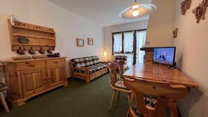 A cozy living room with a wooden dining table, a sofa, and a television. - 071 Bilocale Pinzolo (Pinzolo)