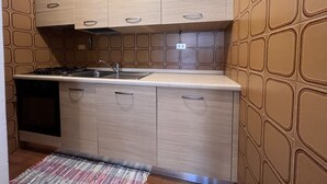 A compact kitchen with wooden cabinets, a stainless steel sink, and a patterned backsplash. - 071 Bilocale Pinzolo (Pinzolo)