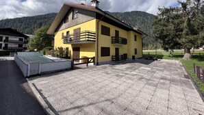 A yellow building with balconies, a paved driveway, and a mountainous backdrop. - 071 Bilocale Pinzolo (Pinzolo)