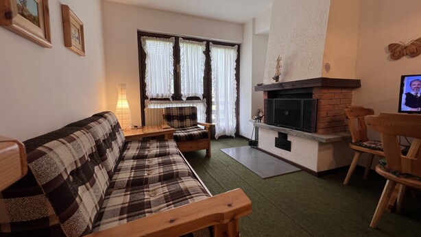 A cozy living room with a sofa, a fireplace, and a television. - 071 Bilocale Pinzolo (Pinzolo)