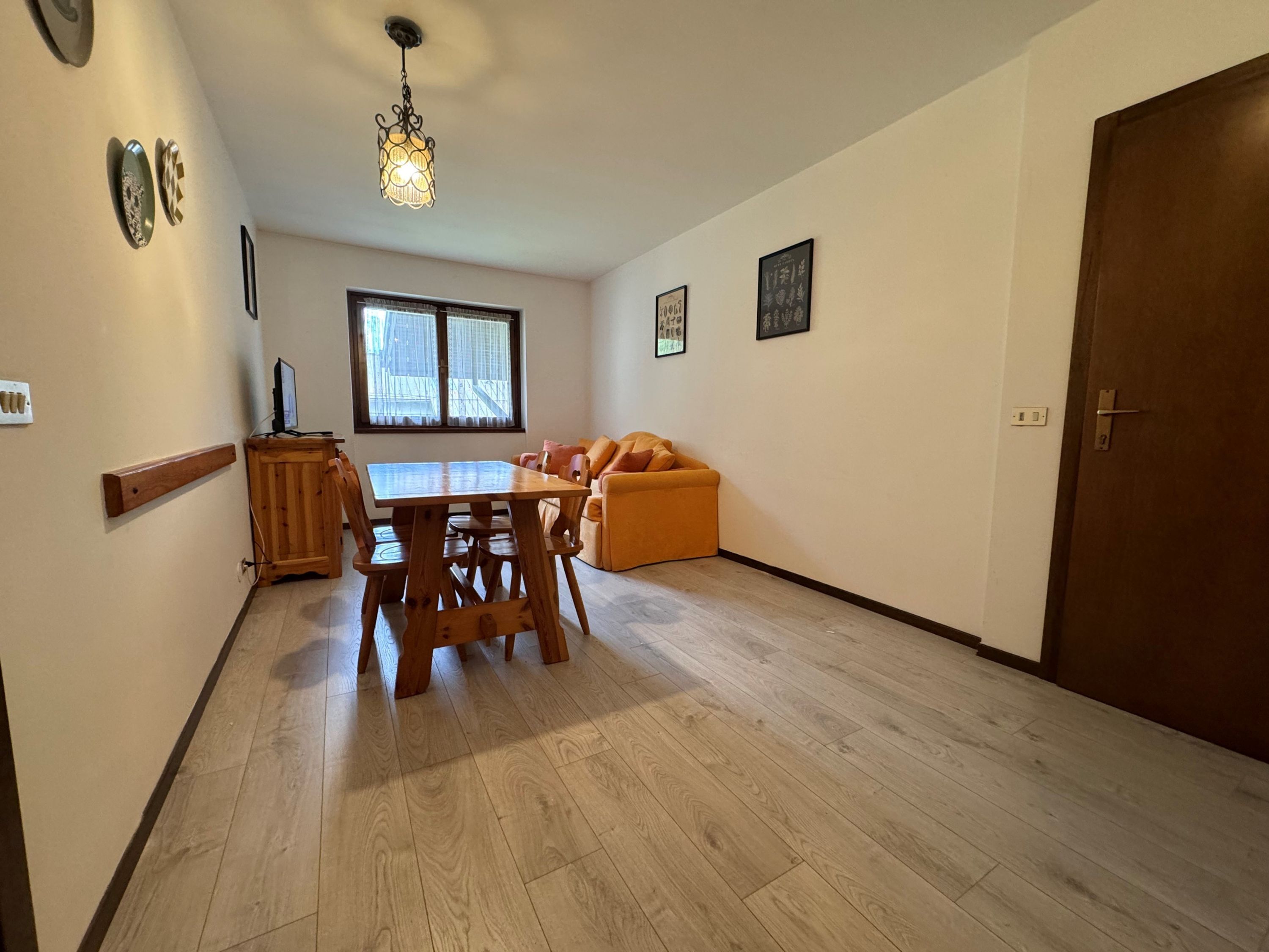 Zona pranzo con tavolo e sedie in legno, un divano e una finestra con persiane.
