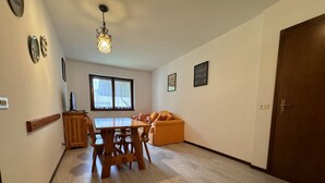 Zona pranzo con tavolo e sedie in legno, un divano e una finestra con persiane.