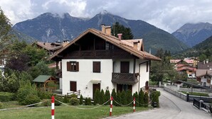 A traditional chalet with a sloped roof, wooden balconies, and a view of a mountain range. - 072 Trilocale Giustino (Giustino)