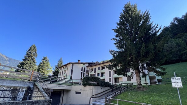 Un edificio con entrada protegida por una reja, una escalera que conduce al cuerpo principal, y un letrero que indica zona de estacionamiento reservada.
