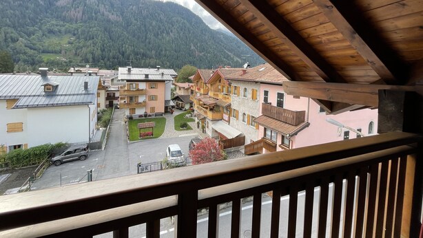 A view from a balcony overlooking a village with traditional buildings, a paved street, and a mountainous backdrop. - 032 Luminosa Mansarda Pinzolo (Pinzolo)