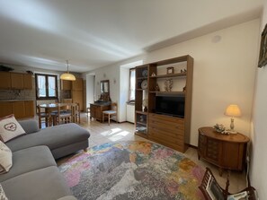 A living room with a sofa, a TV, a wooden cabinet, and a dining area with chairs and a table. - 062 Ampio Trilocale Carisolo (Carisolo)