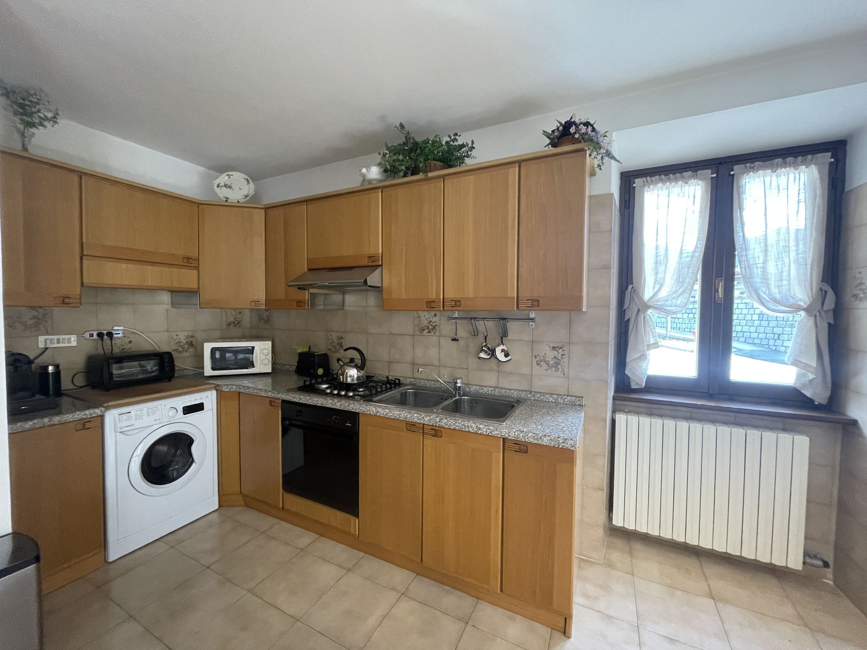 Una cocina compacta con armarios de madera, lavadora, microondas y un lavabo.