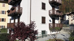 Un immeuble à plusieurs étages doté de balcons, avec un arbre au premier plan et un paysage montagneux en arrière-plan.