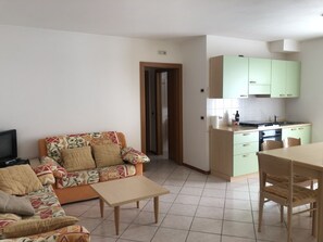 Una sala de estar con un sofá, una mesa de centro y un televisor. Hay una zona de cocina con un fregadero, estufa y armarios.