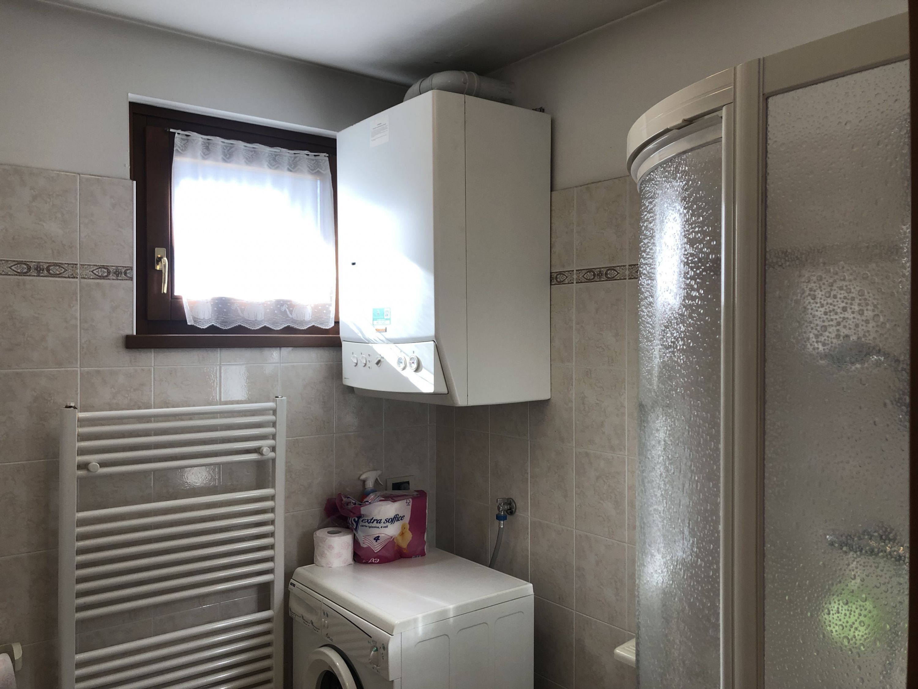 A compact bathroom with a built-in washing machine, a towel rack, and a shower enclosure.