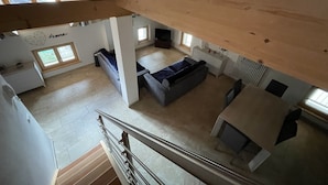 A spacious loft-style living area with a high ceiling and exposed wooden beams. There is a gray sofa, a small table, and a window providing natural light. - 061 Bilocale Mansarda Carisolo (Carisolo)