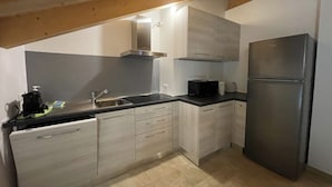 A modern kitchen with light wood cabinets, a stainless steel refrigerator, and a black countertop. - 061 Bilocale Mansarda Carisolo (Carisolo)
