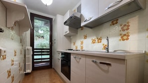 A kitchen with white cabinets, a stove, a sink, and a window with a view of greenery.